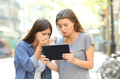 Das Bild zeigt zwei Frauen, die auf ein Tablet starren. Eine der Frauen sieht erschreckt aus, hält die Hand vor den Mund.